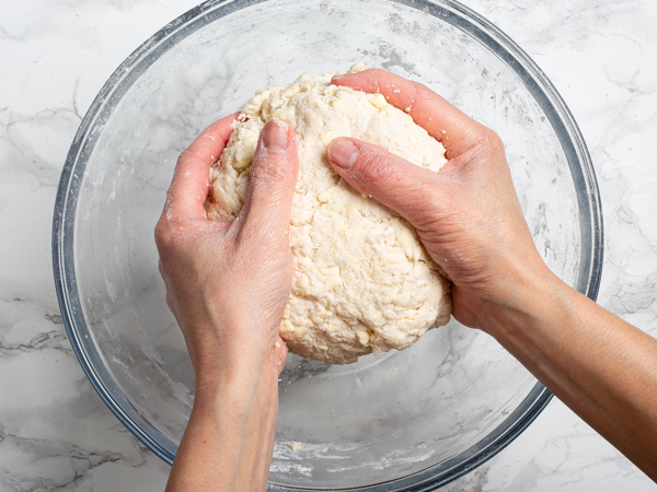 Two hands holding a ball of pie crust dough over a glass bowl