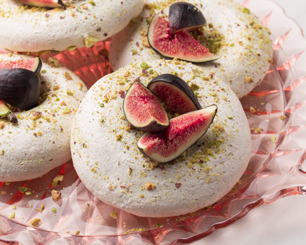 Meringues on a glass dish, topped with pistachio and figs