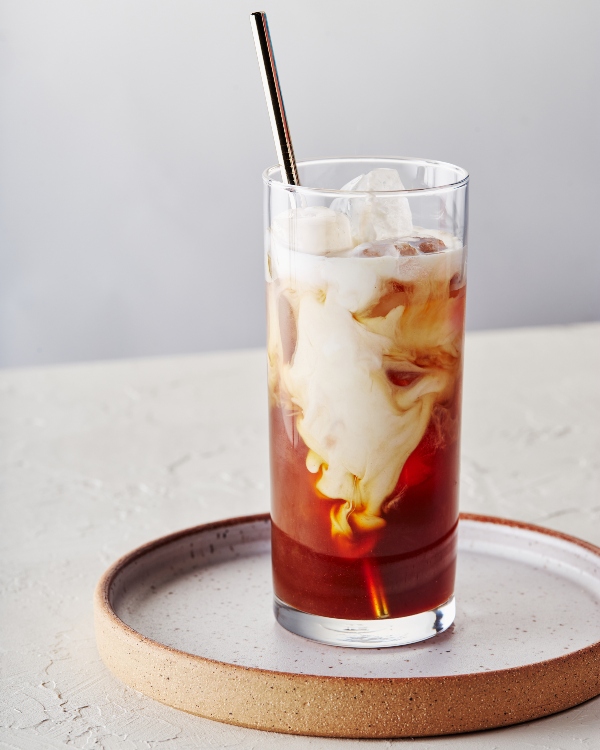 Glass of pumpkin spice cold brew with swirls of cream over ice served with a reusable straw