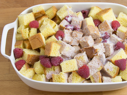 Dish full of bread cubes, cream, and raspberries