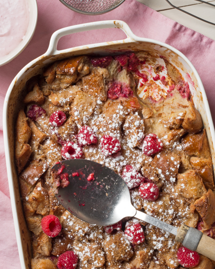 Baking dish full of raspberry bread pudding with a serving spoon