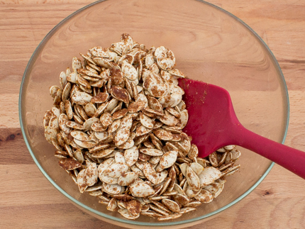 Stirring dry pumpkin seeds with sugar and spices in a glass bowl with a spatula