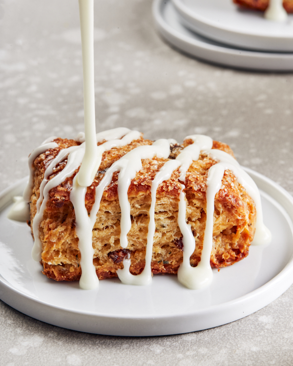 A vanilla rosemary date scone on a white plate with white drizzle icing pouring on top