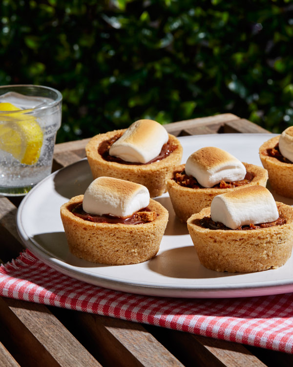 S’mores cookie cups on a platter outdoors shown with a sparkling drink