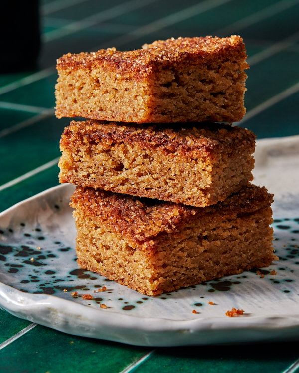 Three snickerdoodle cookie bars in a stack on a speckled platter shown on a green tile counter.