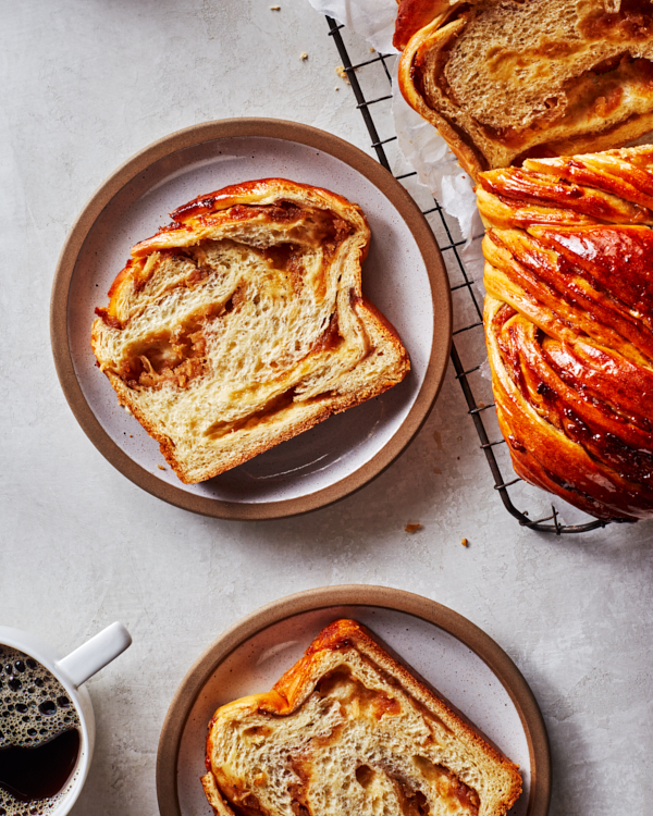 Slices of spiced apple babka on plates shown with the cut loaf on a cooling rack and a mug of coffee