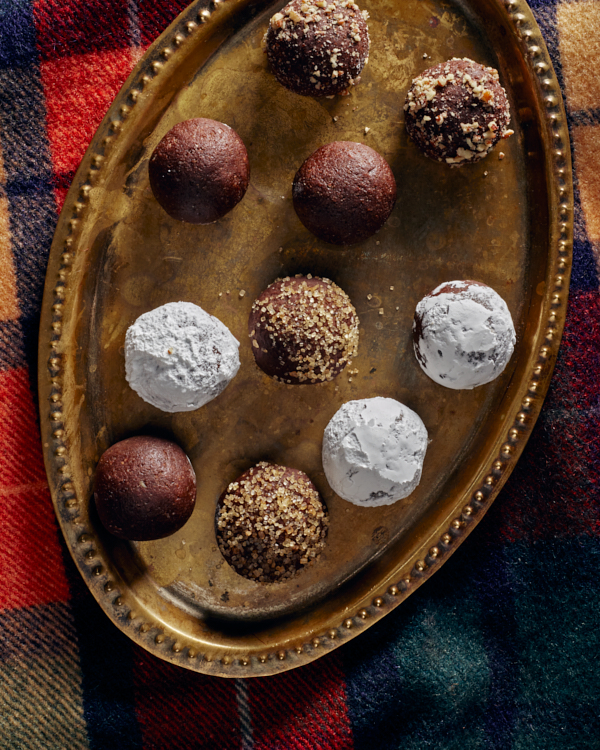 Spiced bourbon balls on a brass platter on a plaid blanket, topped with icing sugar, crushed nuts, and turbinado sugar.