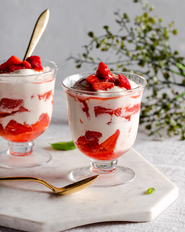 Strawberry fool in two parfait glasses on a marble slab with gold spoons