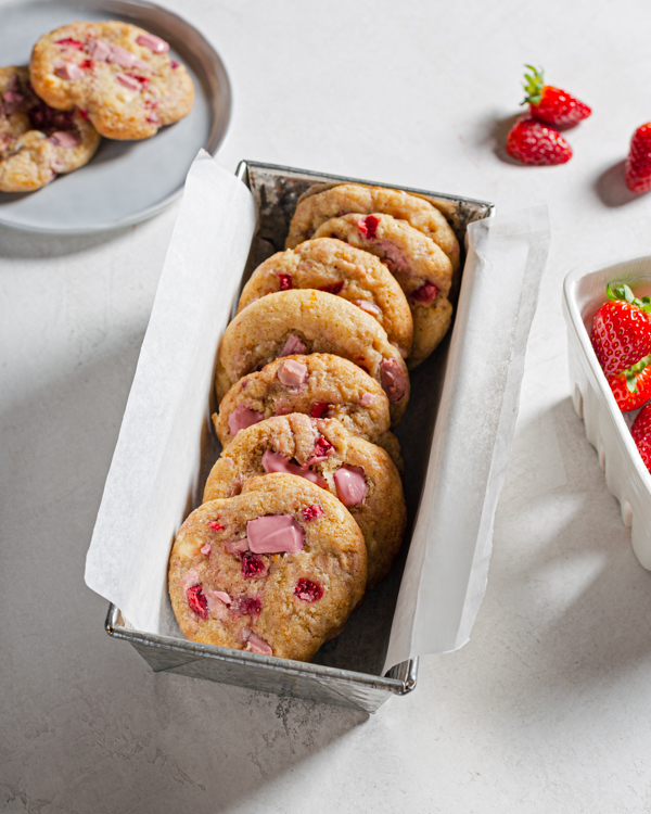 A parchment lined tin filled with strawberry and ruby chocolate chunk cookies