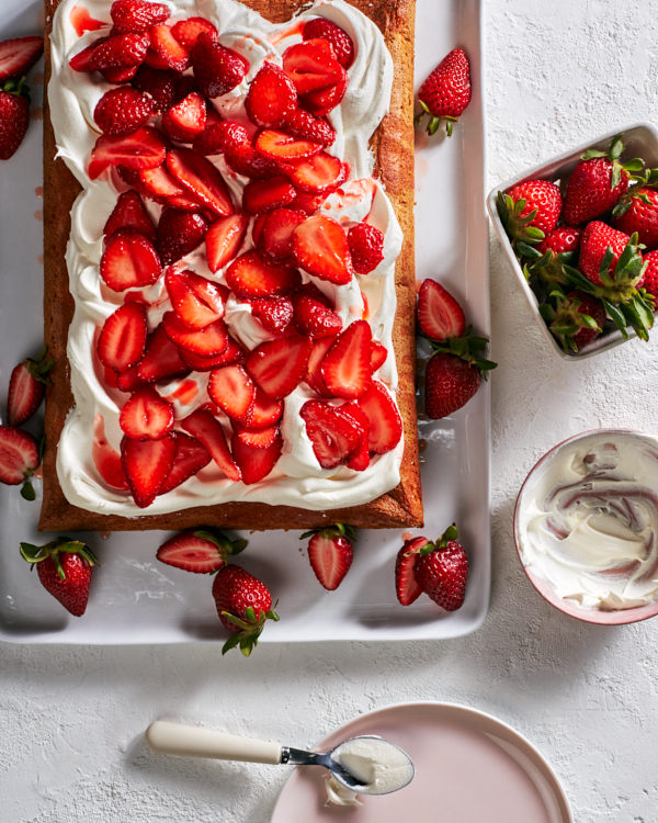 A strawberry-yuzu sheet cake on a white tray served with strawberries and a bowl of frosting.