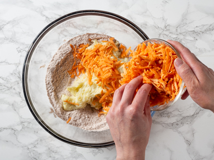 Adding grated sweet potatoes to a bowl of mashed potatoes and dry ingredients