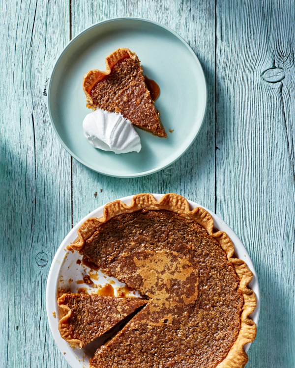 Tarte au Sucre, or sugar pie, in a white pie plate with two slices cut, one served on a pale blue plate with a dollop of whipped cream.