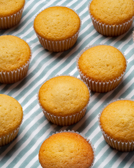 Plain vanilla cupcakes in wrappers resting on a striped tablecloth