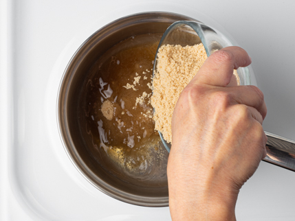 Pouring golden sugar from a glass bowl into a pot of water on a stove
