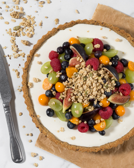 Yogurt Fruit Tart with Granola Crust topped with fruit sitting on parchment paper with a butterknife beside it
