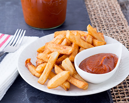 Table setting with plate, napkin and fork. French fries on the plate with ramekin of ketchup. 