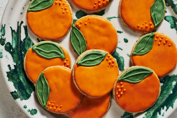 Shortbread cookies decorated to look like oranges on a white and green plate.