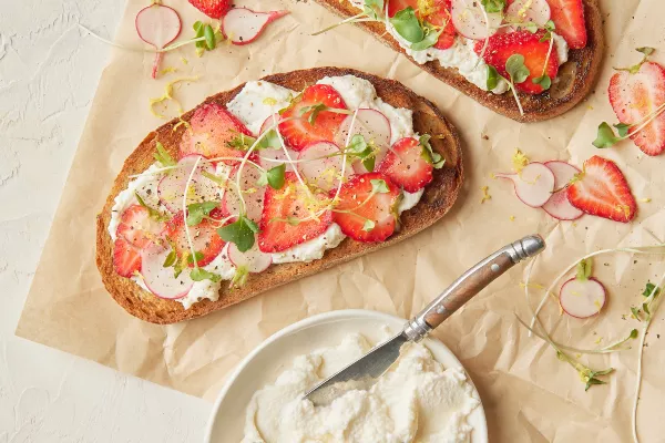 Two slices of toasted bread topped with whipped brown sugar ricotta, sliced strawberries and radishes, and microgreens