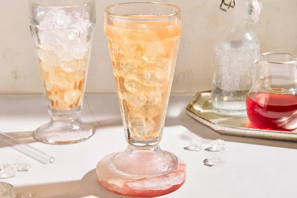 Two parfait glasses of old-fashioned cream soda on ice shown with a bottle of soda and a pitcher of strawberry simple syrup