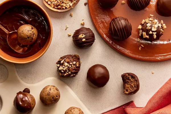 Chocolate-Dipped Cookie Dough Bites in various stages of completion, some sprinkled with nuts, one with a bite missing