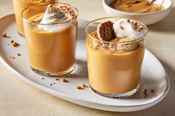 Three glasses of butterscotch pudding on a small oval tray, each topped with whipped cream, toffee bits, and cookies.