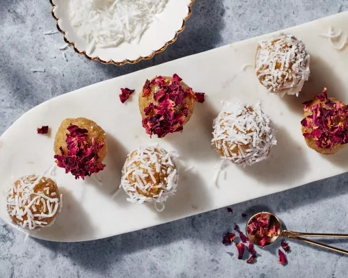 Golden Badam Ladoo garnished with rose petals and coconut on a thin white platter