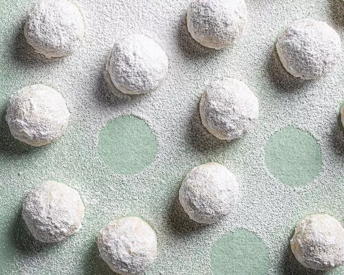 Snowball cookies on a green background, dusted with icing sugar
