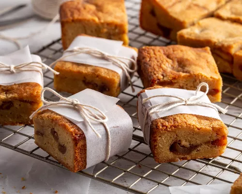 Apple blondies cooling on a wire rack, some wrapped with parchment paper