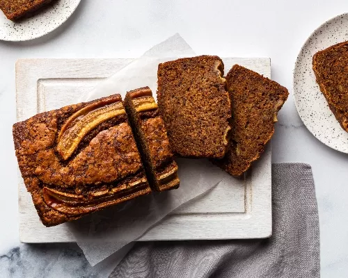 Banana bread on a cutting board with pieces cut and slices on plates