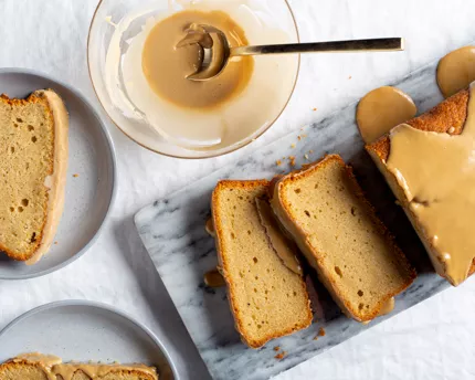 Slices of glazed beer cake on a marble slab with a bowl of glaze and two plated slices