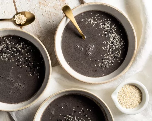 Three bowls of black sesame seed soup garnished with white and black sesame seeds on a wooden table