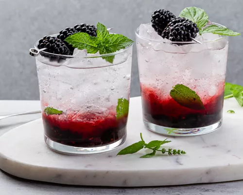 Two blackberry gin fizz cocktails garnished with blackberries and mint leaves on a platter