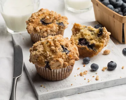 Three blueberry muffins served with milk and a basket of blueberries