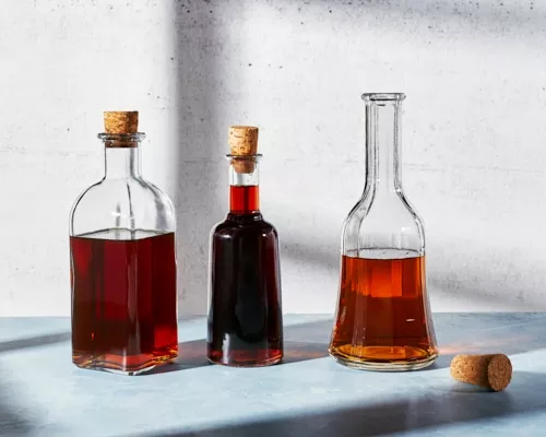 Three glass bottles of brown sugar simple syrup on a counter, two corked and one uncorked