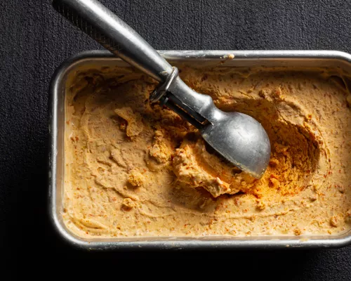 Carrot ice cream in a metal tin with an ice cream scoop