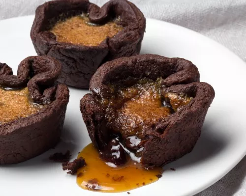 Chocolate Butter Tarts on a plate, one with filling leaking out