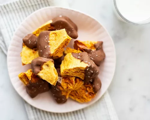 A bowl of chocolate coated sponge toffee on a bowl with a glass of milk