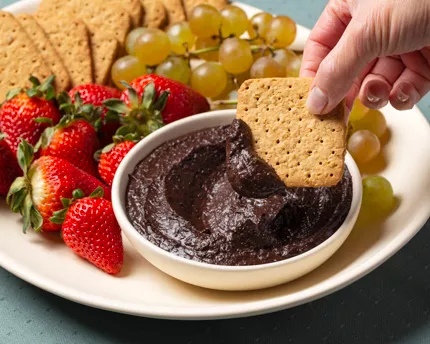 Bowl of chocolate hummus on a platter with graham crackers, figs, strawberries, and grapes