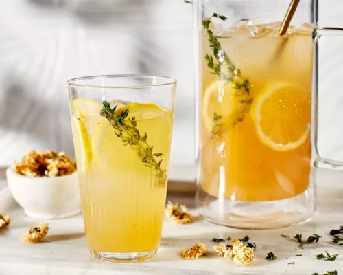 Sparkling chrysanthemum tea lemonade in a glass and a glass pitcher, served with lemon slices and chrysanthemum sprigs and flowe