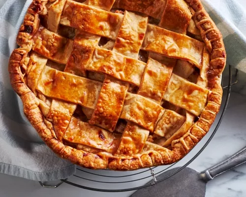 Lattice-topped apple pie on a cooling rack with a pie server
