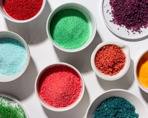 Several bowls of coloured sugar (edible glitter) in different shades and textures