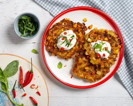Sweet Chili Corn Fritters on a red and white plate with sour cream and herbs