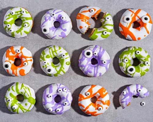 Cinnamon donuts with colourful icing and eyeball candies on a counter