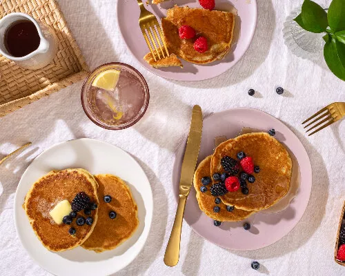 Three plates of easy fluffy pancakes in a picnic setting, with fresh berries, butter and maple syrup