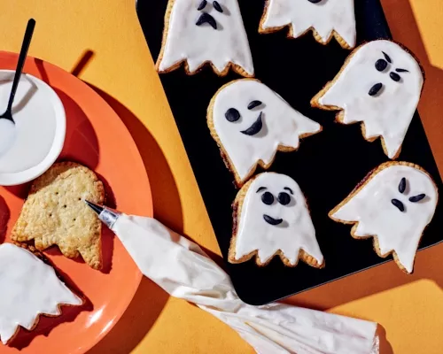 Ghost-shaped tarts, some decorated with black icing faces drawn on white icing, some undecorated