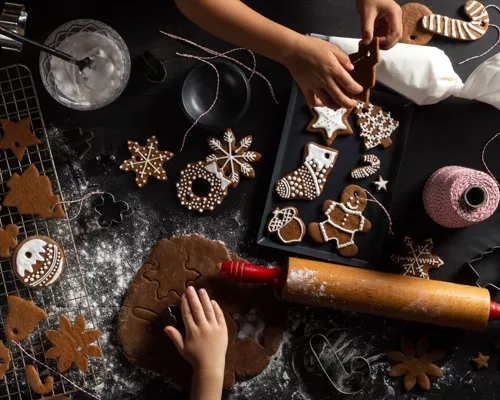 An assortment of gingerbread cut-out cookies on a cooling rack, counter, and pan with icing and decorating equipment