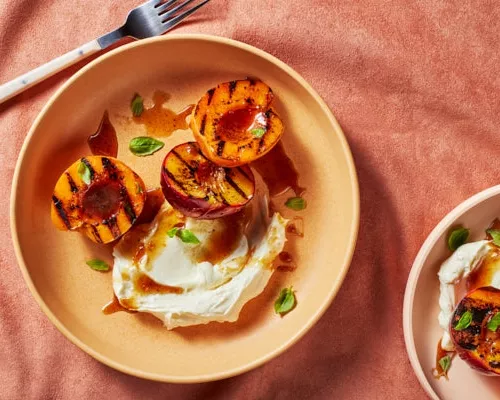 Two bowls of grilled peach halves with mascarpone and basil garnish and brown sugar glaze