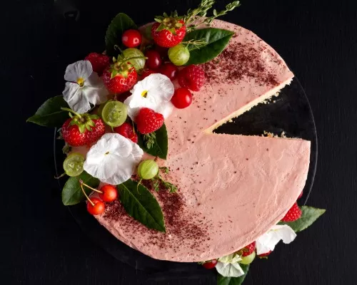 Pink Swiss meringue buttercream frosted cake on a cake stand decorated with flowers, greenery, and berries