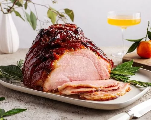 Roasted glazed ham on a platter and garnished with herbs with several slices cut
