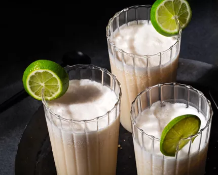 Three glasses of coconut kombucha garnished with lime slices on a black plate